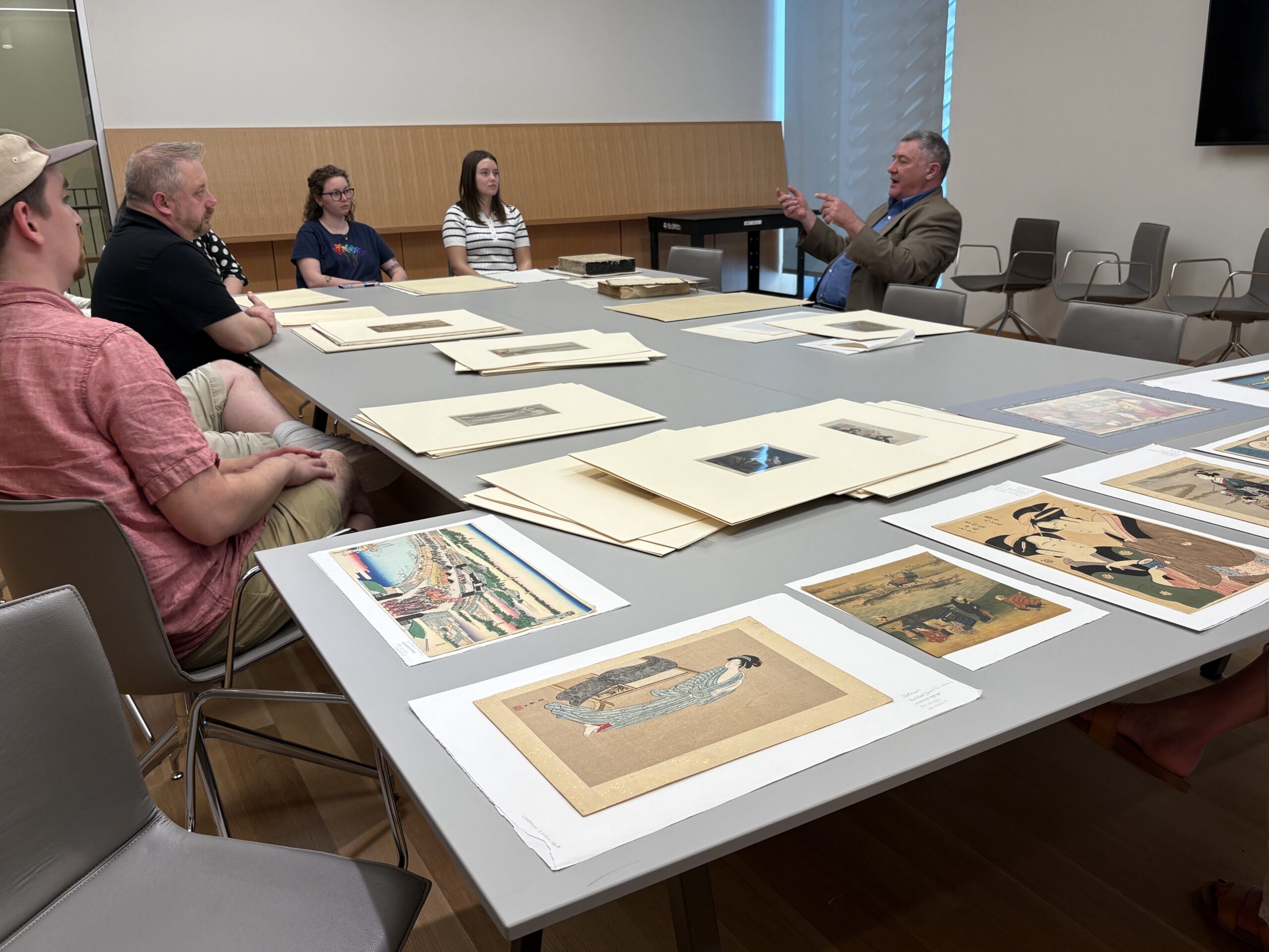 A group of people around a table with artworks on paper laid out to look at.